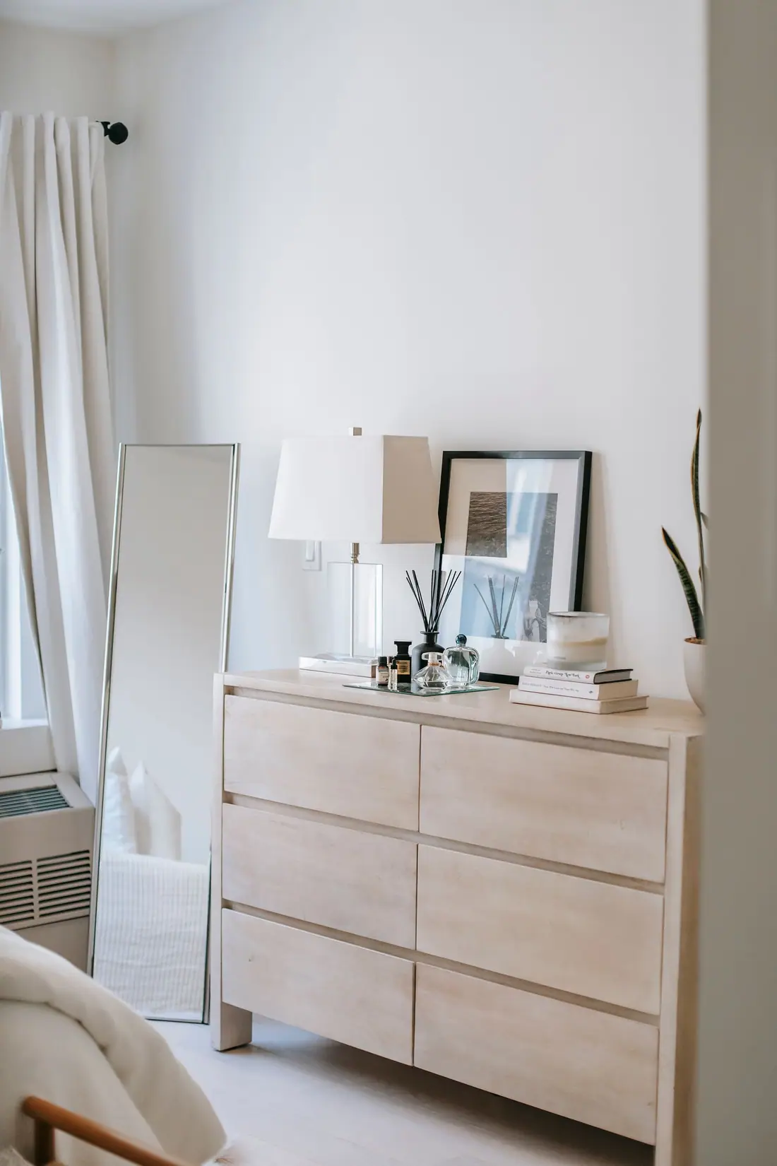 Six-drawer light wood dresser against a white bedroom wall, with a mirror leaning beside it