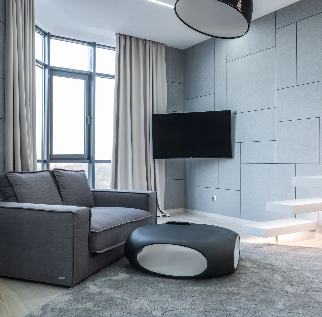 Gray sofa facing a wall-mounted television in a room with a large window