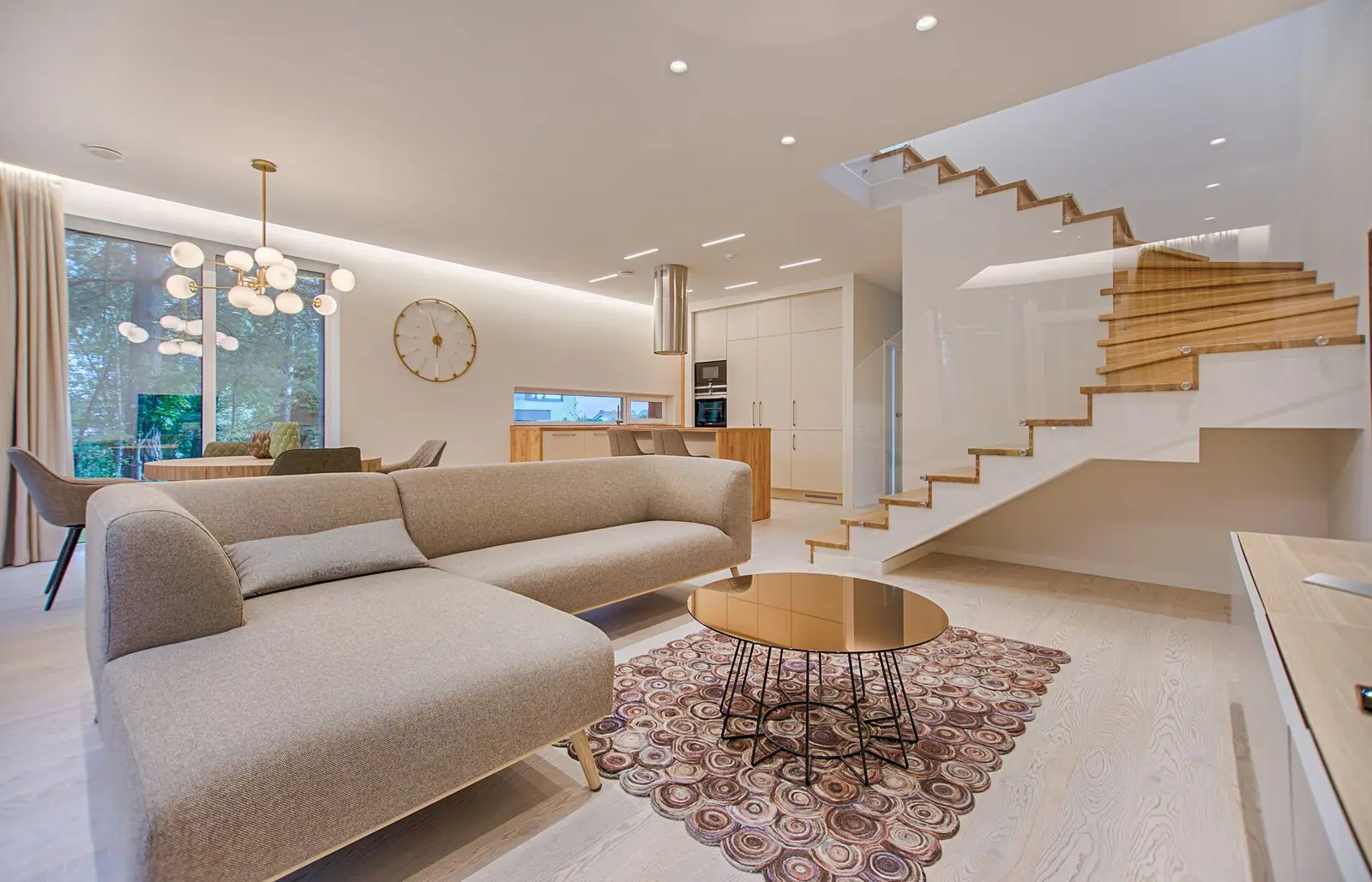 Light living room with a beige sectional, a round coffee table, and an open stair
