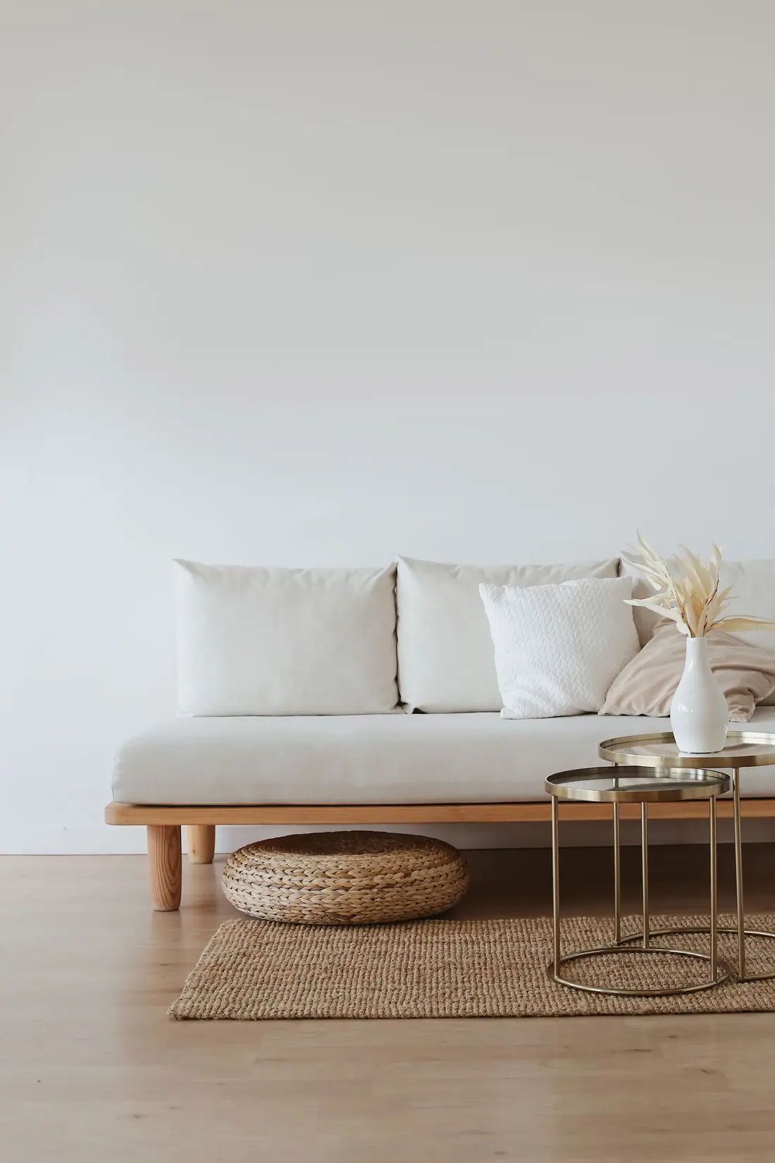 Low sofa with light cushions, a woven rug, and nested metal tables