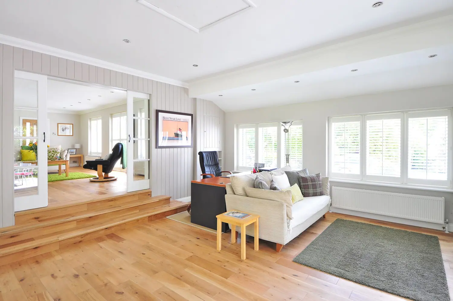 Sunlit living room with wooden steps, French doors, and a sofa along the window wall