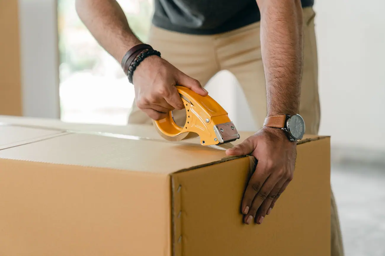 Hands sealing a cardboard carton with a yellow tape dispenser